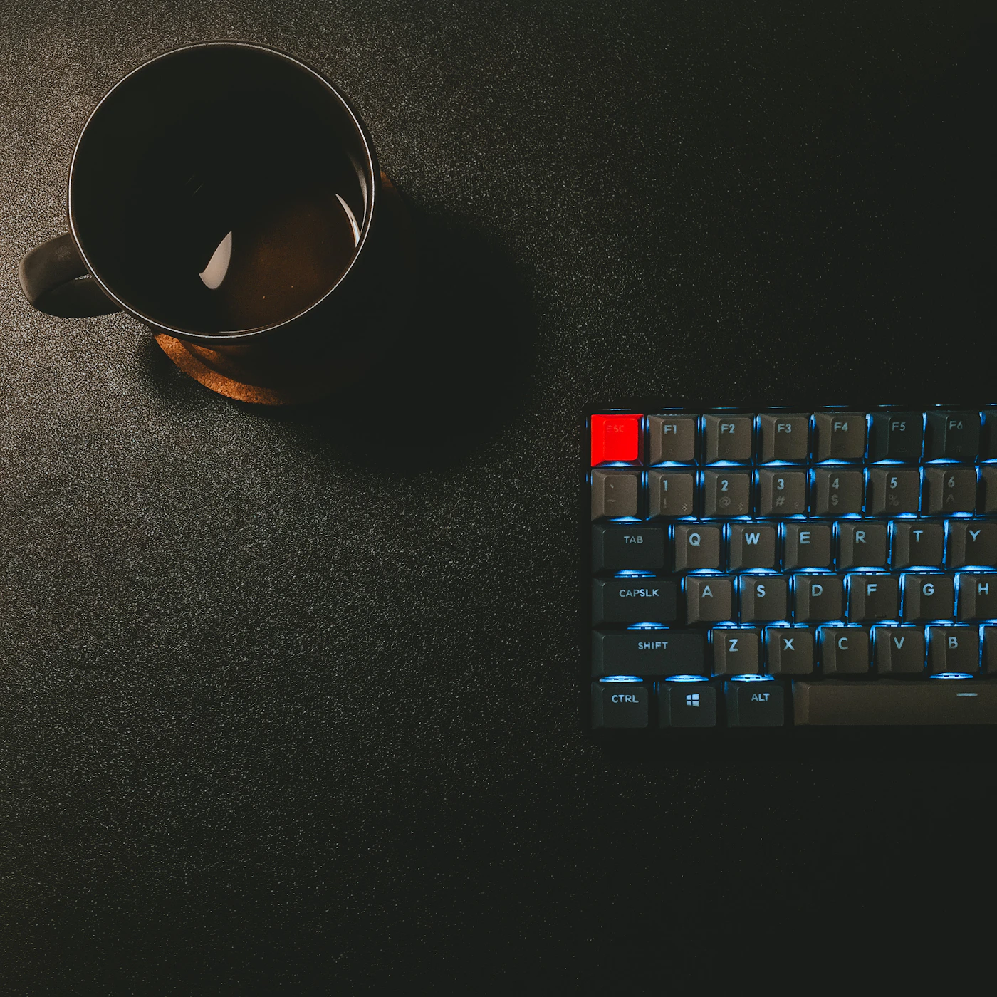Black coffee beside a keyboard on a dark desk